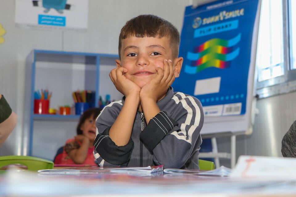 A child smiles during an educational activity at at a UNICEF -supported early childhood learning center in Ain Khadra camp in Al-Malikiyeh, Al-Hasakeh, Syria.